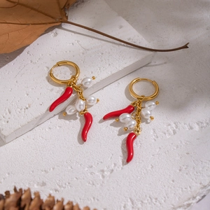 Detail of gold red chili and pearl drop earrings on white stone with autumn leaves