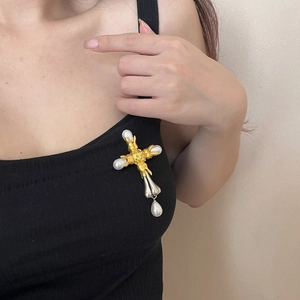 Detail of vintage bicolor cross brooch with pearls worn on model against black background
