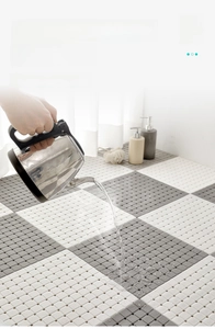 Detail of grey and white TPE interlocking shower mat showing 100°C heat resistance