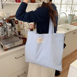 Blue striped canvas tote bag shown worn by a model in a cozy coffee shop setting