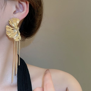 Detail of golden ginkgo leaf earrings with long chain tassels worn by a model
