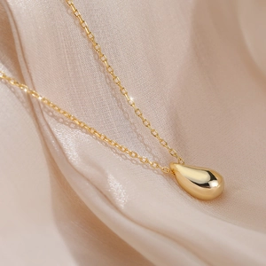 Polished gold s925 sterling silver teardrop pendant necklace on silk fabric background