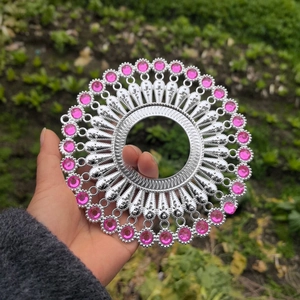 Macro shot of silver circular metal ornament with radial patterns and pink gemstones