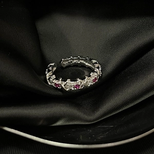 Close-up of silver adjustable ring with red and white gems on black silk fabric