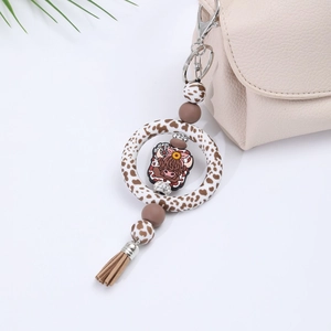 Detail of highland cow car charm with leopard print ring and brown tassel on beige bag