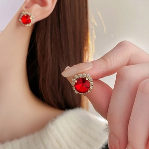 Detailed close-up of French-style gold earrings with round red gems and halo crystals