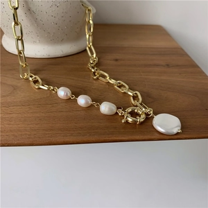 Detail of gold rectangular chain with baroque pearls and OT toggle clasp on a white jar