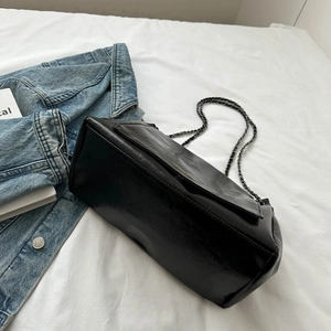 Glossy black leather chain shoulder bag displayed on a white bed with lifestyle props
