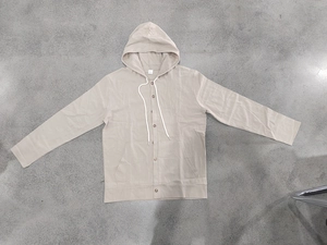 Flat lay of a beige hooded linen shirt with buttons, white drawstrings and side pockets