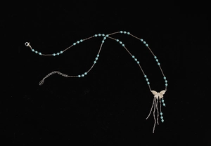 Detailed close-up of blue beaded butterfly necklace with steel tassels and logo tag