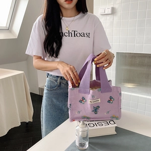 Close-up of purple canvas lunch bag with colorful butterfly embroidery and white woven label