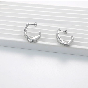 Macro shot of silver geometric earrings with irregular hammered texture on white stand