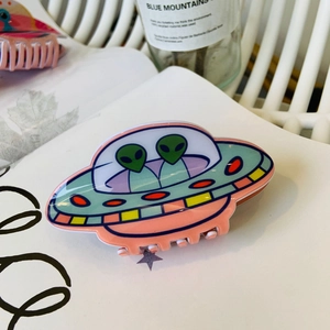 Pink acrylic UFO alien hair claw clip with colorful cartoon space design on a white desk