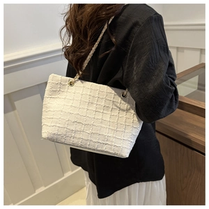 Detailed macro view of white tweed tote bag with gold chain strap and textured weave fabric