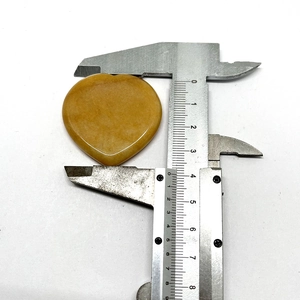 Macro shot of a yellow heart-shaped massage stone measuring 40mm on a caliper scale