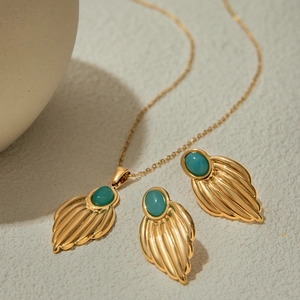 Detail of gold titanium steel necklace and earrings with green oval gemstone leaves