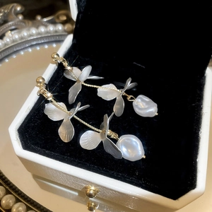 Detail of long gold tassel earrings with frosted petals and baroque pearls in a jewelry box