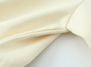 Dettaglio ravvicinato di cuciture e trama del tessuto a maglia sulla felpa color crema