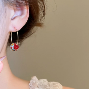 Close-up of a gold hoop earring featuring a transparent resin bead with colorful dots