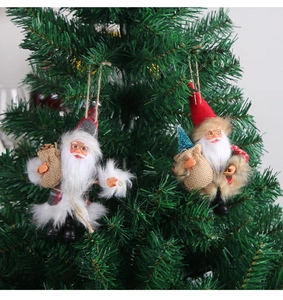 Close-up of Santa and elf plush ornaments hanging on green Christmas tree branches