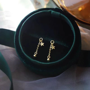 Macro shot of gold star tassel chain earrings with bead detail in a green velvet jewelry box