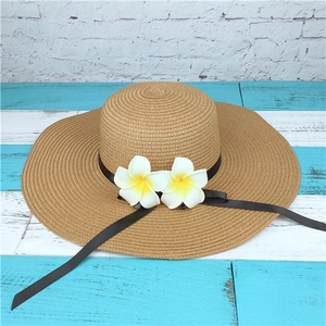 Detail of natural wide-brim straw hat featuring black ribbon and yellow frangipani flowers