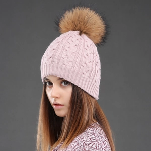 Detail of pink cable knit winter hat for women featuring a fluffy brown faux fur pom-pom