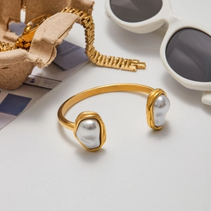 Détail d'un bracelet ouvert en acier titane doré avec perles baroques et accessoires