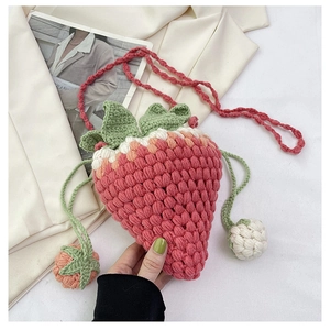 Detailed close-up of handmade red strawberry crochet bucket bag with mini charms