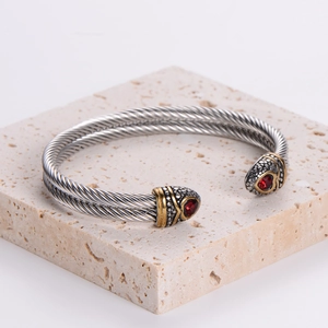 Two-tone cable twist open bangle with red gemstones on a stone pedestal display
