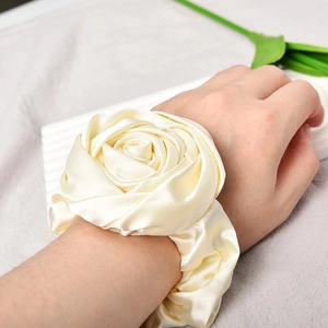 Detail of cream white satin rose scrunchie worn on wrist with silky floral texture