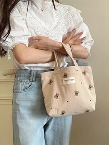 Beige corduroy tote bag with bear embroidery carried by model in casual outfit