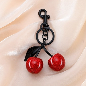Detail of red glitter cherry charm pendant with black metal clip on beige silk fabric