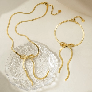 Gold stainless steel snake chain jewelry set with bow pendants on a textured glass plate
