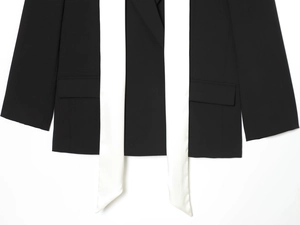Détail d'un blazer noir avec rubans de satin blanc contrastés et texture mate du tissu