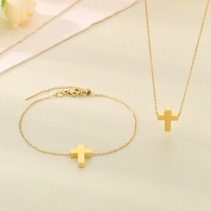 Detailed view of golden cross pendant necklace and bracelet set on soft beige fabric