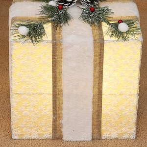 Close-up of white plush Christmas gift box with gold mesh ribbon and warm LED lights