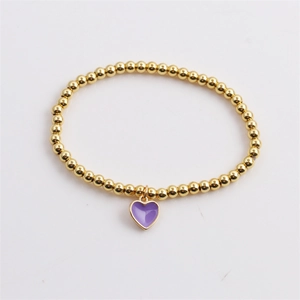 Close-up of golden beaded stretch bracelet with purple heart enamel charm on white background