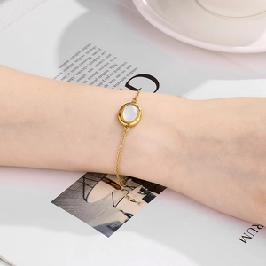 Detailed view of an oval white shell gemstone on a gold chain bracelet worn by a model