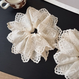 Elegant beige lace embroidered scrunchie with floral cutouts on dark wood background
