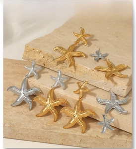 Detailed view of gold and silver starfish drop earrings on natural stone surface