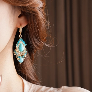 Détail de boucles d'oreilles bohèmes dorées avec pierres turquoise et glands en perles