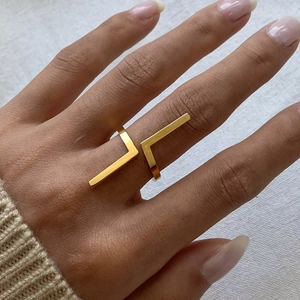 Detail view of a golden irregular geometric open ring worn on a finger over white fabric