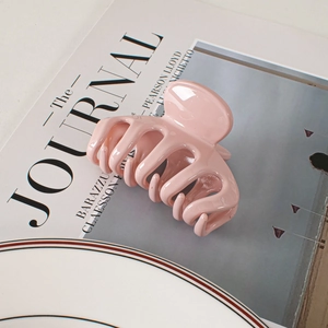 Detail view of a glossy pink hair claw clip placed on a magazine with soft natural lighting