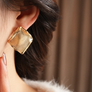 Gros plan de boucles d'oreilles carrées plaquées or avec texture tissée sur modèle