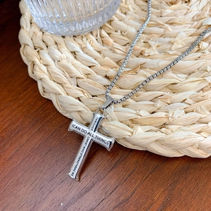 Silver stainless steel cross necklace with religious verse on a rustic woven mat