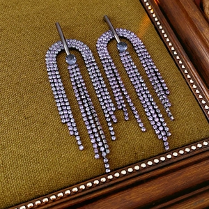 Macro detail of purple rhinestone fringe earrings on olive brown textured fabric background