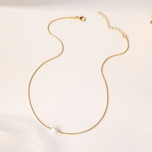 Detail of a gold snake chain necklace with a white pearl pendant and lobster clasp