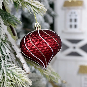 Burgundy heart-shaped Christmas ornament with diamond texture on a snowy pine branch
