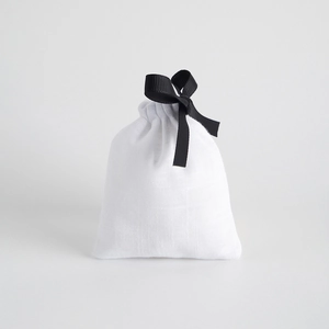 Close-up of white cotton drawstring bag with black ribbon bow and fabric texture detail